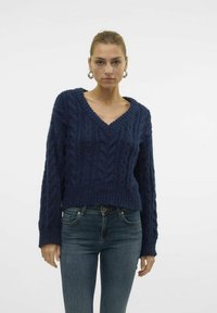 Navy blue knitted sweater with a V-neck, textured cable pattern, and long sleeves, paired with dark blue jeans.