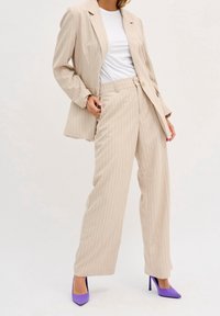 Béžový pruhovaný sako a kalhoty s širokými nohavicemi, kombinované s bílým tričkem a fialovými podpatky. Hladká textura, přizpůsobený design.