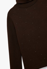 Brun turtleneck top lavet af blødt stof, med et tekstureret design og spredte sorte perler på forsiden.