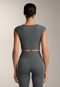 Šedá žebrovaná souprava sportovního oblečení obsahující zkrácený top s krátkými rukávy a legíny s vysokým pasem, obojí s jemnými detaily značky.