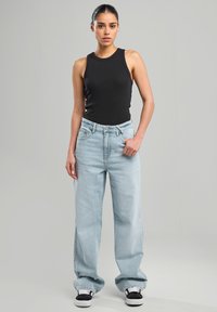 Black sleeveless top paired with light blue baggy jeans. The jeans have a high waist and are styled with black and white sneakers.