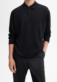 Schwarzes langärmliges Polohemd mit Kragen, entspannter Schnitt und Knopfverschluss mit vier Knöpfen. Glatte Stofftextur, getragen mit schwarzen Hosen.