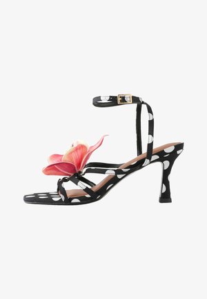 Fekete-fehér pöttyös magas sarkú szandál boka pánttal és nagy rózsaszín virág díszítéssel az elülső pántokon.