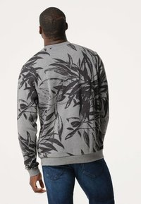 Grijze sweatshirt met zwarte bladerenpatronen, ronde hals en geribbelde manchetten. G gedragen over blauwe jeans, met een relaxte pasvorm en zachte textuur.