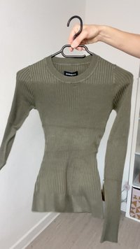 Olivengrønn ribbestrikket langermet topp med rund halslinning. Laget av teksturert stoff, har den en tettsittende silhuett og en lett stretch.