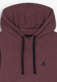 Sudadera con capucha color granate que presenta una capucha grande y ajustable. Cordones de color azul marino oscuro y un pequeño logo de calavera y tibias cruzadas en el pecho. Textura suave.