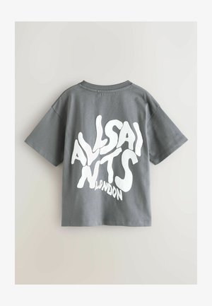 Siva bombažna majica s kratkimi rokavi, z velikim belim stiliziranim napisom na hrbtni strani. Ohlapne prileganje in gladka tekstura.