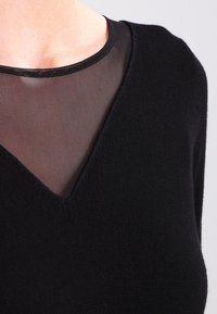 Mustapaita, jossa on V-pääntie, valmistettu pehmeästä kankaasta ja jossa on läpinäkyvä verkko-osa pääntiellä, mikä lisää rakennetta ja visuaalista kontrastia.