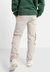Beige cargobroeken met een recht model, voorzien van zij- en achterzakken, gemaakt van duurzaam materiaal. Draag ze met een groene sweatshirt en sneakers.
