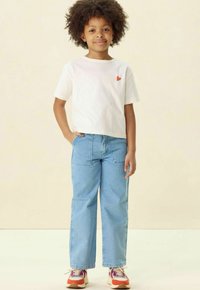 Witte t-shirt met korte mouwen en een rood hartlogo, gecombineerd met lichtblauwe rechte jeans en multicolore sneakers.