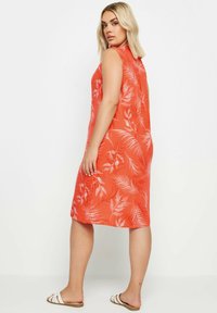 Röd ärmlös klänning med vitt bladmönster, knälång, rak skärning, gjord av lätt tyg; ihop med vita sandaler.