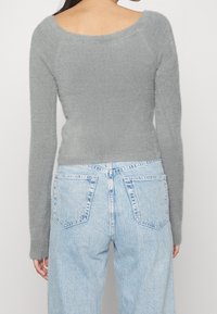 Grijze, fuzzy trui met lange mouwen en een brede halslijn, gecombineerd met lichtblauwe, high-waisted jeans met achterzakken.