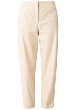 Person iført beige bukser, hvide sneakers og en hvid cropped jakke med sort ternet mønster, går på en neutral baggrund.