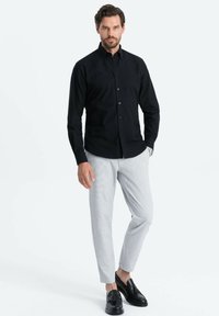 Camicia nera con bottoni e maniche lunghe, abbinata a pantaloni grigi chiari a motivo e mocassini neri. Texture morbide e vestibilità su misura.