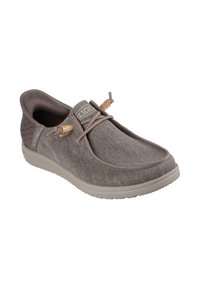 Zapato gris sin cordones con tela texturizada, suela de goma y cordones elásticos. Presenta una puntera suave y redondeada, con acentos marrones, incluidos pequeños cierres de madera.