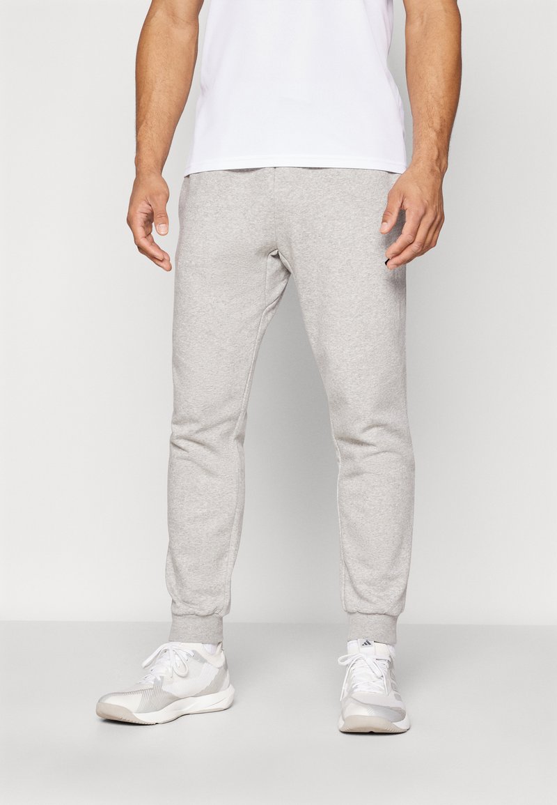 Grå bomulds sweatpants med elastiske manchetter, sidelommer og en afslappet pasform, parret med hvide atletiske sko.