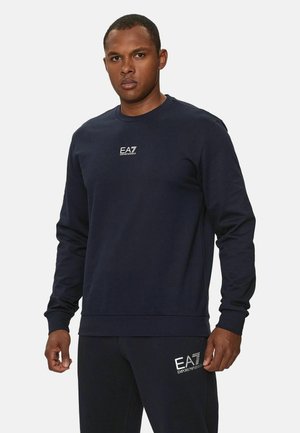 Felpa blu navy con maniche lunghe, collo tondo e logo EA7 ricamato sul petto. Realizzata in un tessuto morbido e strutturato.