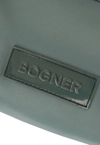 Tessuto in nylon verde con una finitura texture presenta un distintivo patch rettangolare in rilievo con la scritta "BOGNER."