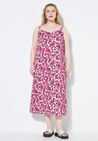 Abito maxi floreale con base bianca, caratterizzato da motivi di foglie e animali in rosa. Spalline larghe e vestibilità rilassata, abbinato a sandali con plateau neri.