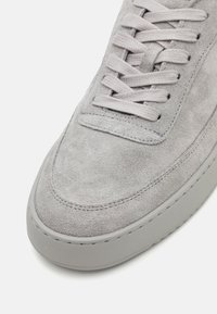 Sneaker in suede grigio con texture liscia, lacci grigi piatti, punta arrotondata e una suola in gomma spessa caratterizzata da un delicato dettaglio a punto.
