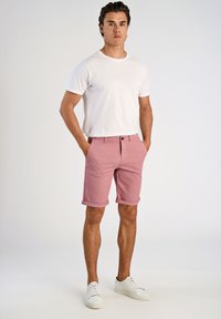 Shorts di cotone rosa con risvolti, chiusura con bottone e zip, abbinati a una maglietta bianca a girocollo e sneaker bianche.
