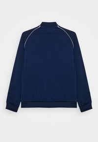 Námořnicky modrá sportovní bunda s vysokým límcem, dlouhými rukávy a bílým lemováním podél švů na ramenou. Hladká tkanina, elastické manžety a spodní lem.