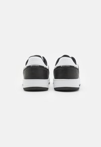 Pantofi sport alb-negru cu un superior din piele netedă, accente texturate, formă rotundă și o talpă din cauciuc cu un model de herringbone.