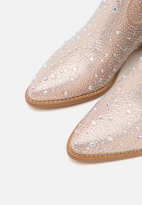 Boty s špičatou špičkou, které mají jemně růžový texturovaný povrch zdobený barevnými krystaly a korálky, s hnědou podešví.