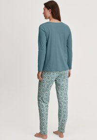Chemise turquoise à manches longues avec un col rond, associée à un pantalon léger bleu à motif floral blanc et vert.