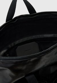 Černý interiér tašky s zipovým otvorem, hladká kůže, černé podšívání a viditelná embosovaná značka.