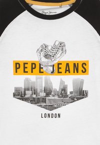 Bílý tričko s černými raglánovými rukávy; má grafiku tenisek a černobílého londýnského panoramatu. "PEPE JEANS" tučným žlutým písmem.