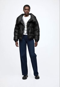 Must turesõjakas jakk kõrge kraega, kombineeritud triibulise valge ja mereväesinise kampsuniga ning tumelõuad tumelillade laiade teksadega. Mustad robustsed kingad.