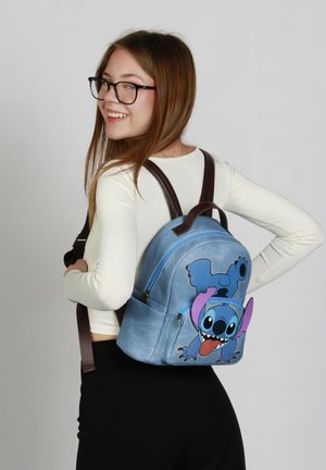 Mochila de color azul claro con diseño del personaje Stitch, correas marrones, bolsillos con cremallera y una textura suave.