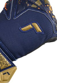 Guanto sportivo blu con tessuto testurizzato, dettagli dorati, motivi geometrici e una sezione del grip rinforzata. Logo visibile sul tessuto.