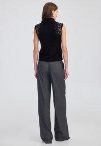 Czarny bezrękawnik z golfem o puszystej teksturze, zdobiony ćwiekami na ramionach. W zestawie z szarymi szerokimi spodniami.