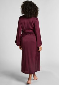 Μακρύ μπορντό μανδύα με υφή και πτυχώσεις, διαθέτοντας φαρδιά μανίκια και αντίστοιχο ζώνη στη μέση. Μαλακό, ρέον ύφασμα.