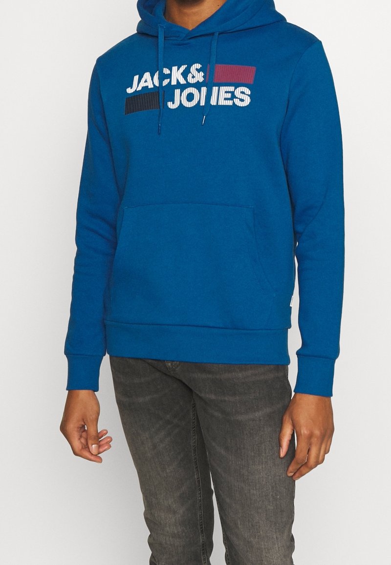 Modrá mikina s kapucí, s přední kapsou typu klokanka. Na přední straně je nápis "JACK & JONES" potištěný bílými a barevnými pruhy.