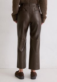 Bruine leren broek met een rechte snit, voorzien van een hoge taille, twee achterzakken en een subtiele glans. Gekozen in combinatie met bruine instappers.