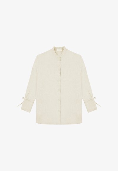 Button-up shirt in light beige linen with a stand collar, long sleeves, and tie accents at the cuffs. Textured, breathable fabric.