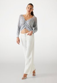 Light gray knit top with openwork pattern, cropped design, and drawstring detail, paired with white wide-leg trousers and silver sandals.