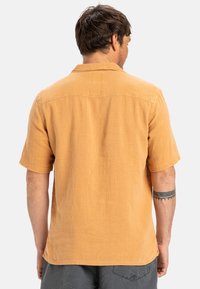 Short-sleeve shirt in mustard yellow, made from a textured fabric; features a spread collar and a straight hem with side slits.