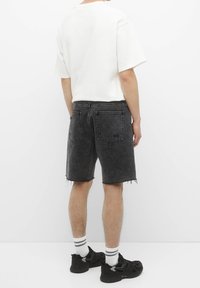 Shorts en denim noir avec ourlet effiloché, cinq poches et coutures contrastées, assortis à un t-shirt blanc ample et des baskets noires.