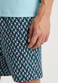 Heren zwemshorts in marineblauw, voorzien van een geometrisch patroon van driehoeken in wit en teal. Gemaakt van lichtgewicht, ademend materiaal.