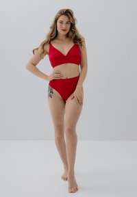 Czerwony zestaw bikini z dekoltem w serek, szerokimi ramiączkami i wysokimi majtkami, wykonany z gładkiego materiału o miękkiej struktury.