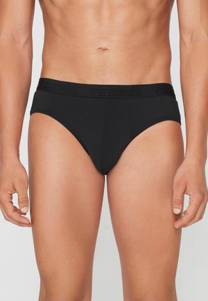 Männlicher Oberkörper, der schwarze Slips mit breitem Bund trägt, gebrandet mit "Tezenis" vor einfarbigem Hintergrund.