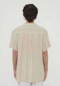 Camicia a maniche corte in un tessuto beige chiaro con righe verticali. Vestibilità rilassata, dettagli del colletto e una consistenza morbida.