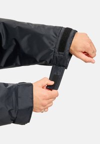 Zwarte geïsoleerde jas met een stoffen textuur, voorzien van een klittenbandriem bij de manchetten voor een verstelbare pasvorm.
