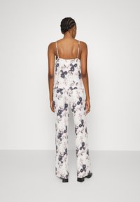 Haut en soie à motif floral avec des fines bretelles, accompagné d'un pantalon large assorti aux couleurs pastel douces, avec une texture lisse.
