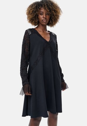 Czarna sukienka z długimi koronkowymi rękawami, dekoltem w szpic i rozkloszowanym dołem. Koronkowe detale z przodu dodają faktury i atrakcyjnego wzornictwa.