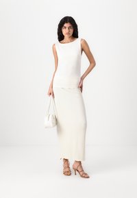 Λευκή χωρίς μανίκια μπλούζα, κρεμ φούστα maxi με υφή, λευκά τσάντα και κομψές καφέ σανδάλια. Απλές, κομψές γραμμές και ουδέτερα χρώματα.